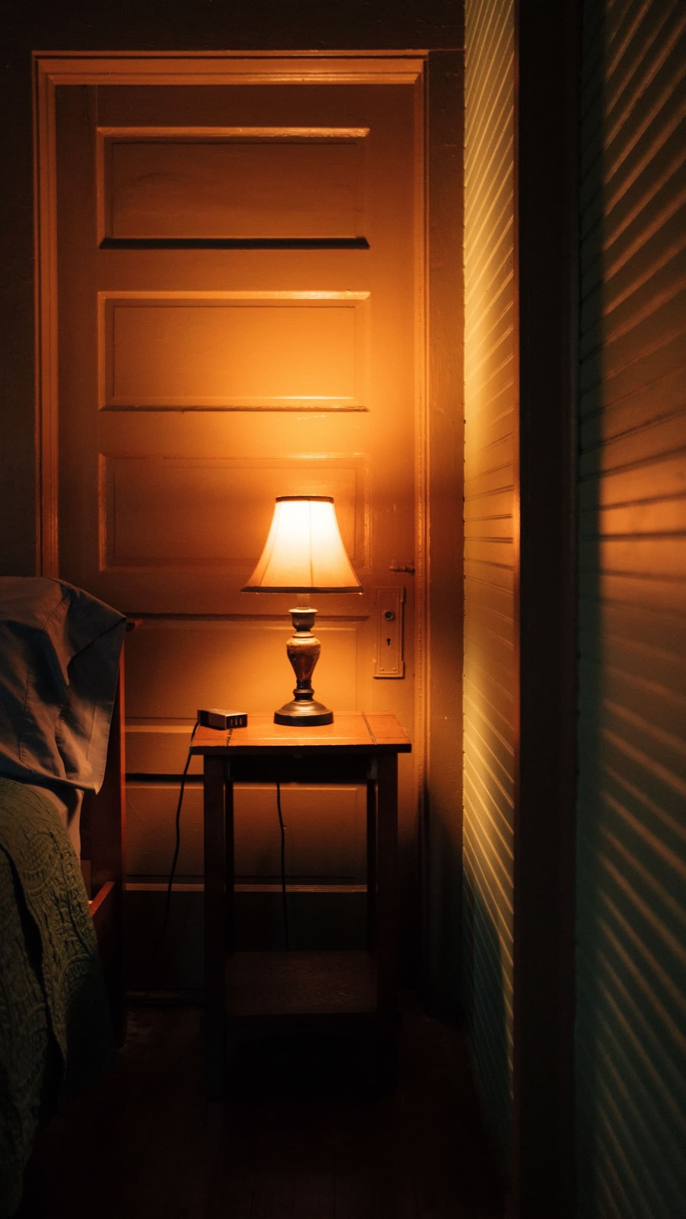 A single lamp left on low beside a bedroom door at night.
