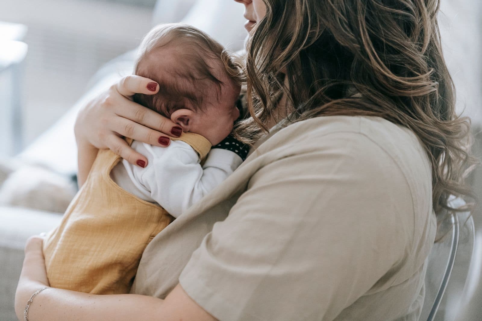 A mother holds her newborn against her shoulder, turned away from the camera.