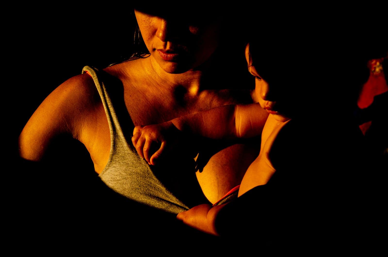 A mother holds her newborn in one warm shaft of light in a dark room.