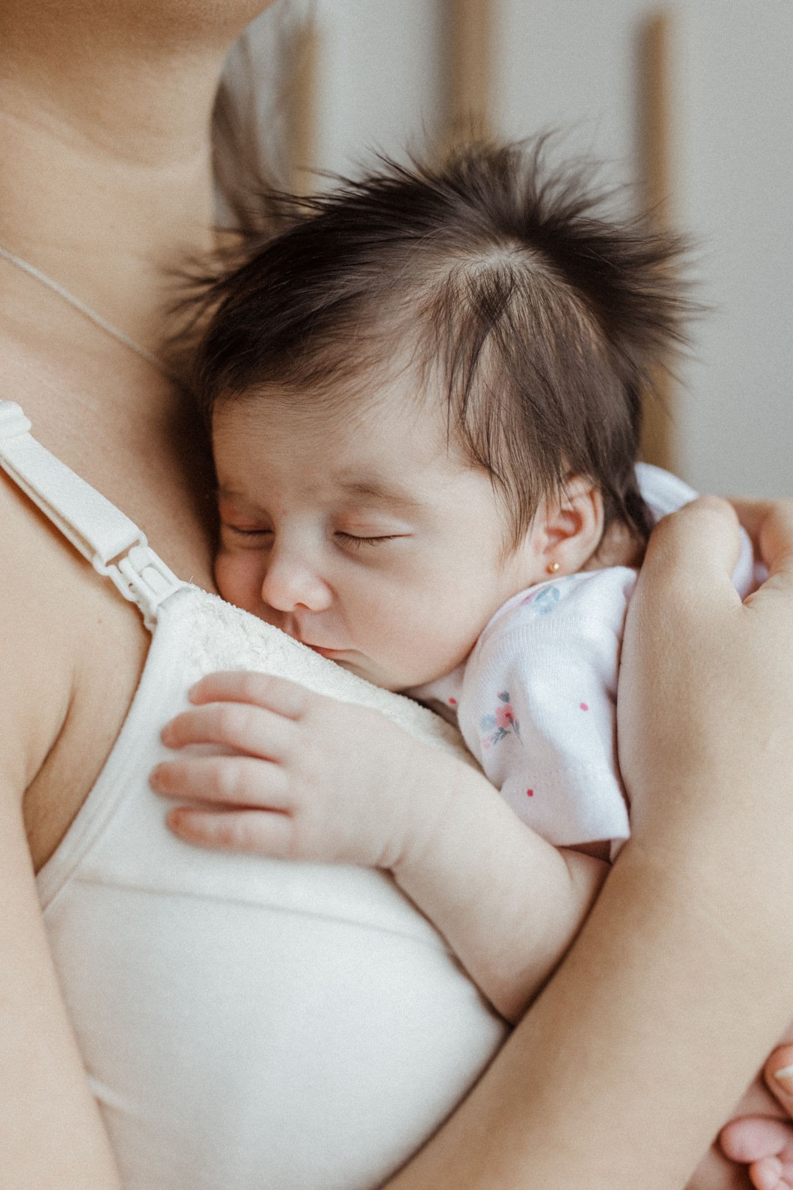 A newborn asleep in his mother's arms, held against her chest.