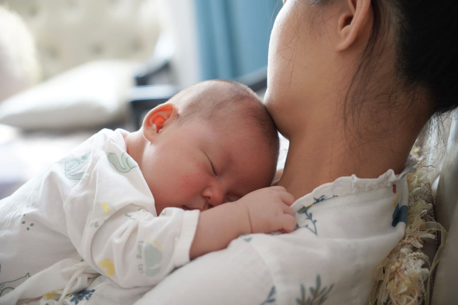 A newborn asleep on his mother's chest in soft window light.